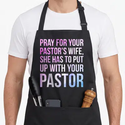 Sarcastic wife apron - Stacked pink purple and blue text reading PRAY FOR YOUR PASTOR'S WIFE — shown on a black cotton canvas apron against a white background