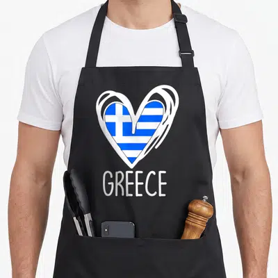 Greece patriotic apron - Blue and white heart containing Greek flag stripes and cross above GREECE text — shown on a black cotton canvas apron against a white background