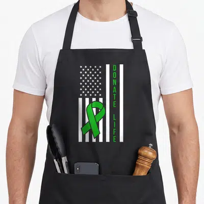 Flag organ apron - Green Donate Life ribbon over white US flag with vertical green text — shown on a black cotton canvas apron against a white background