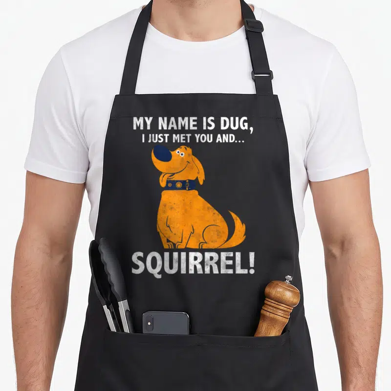 Dug mets apron - Orange dog centered between white distressed text reading My Name Is Dug I Just Met You And Squirrel — shown on a black cotton canvas apron against a white background