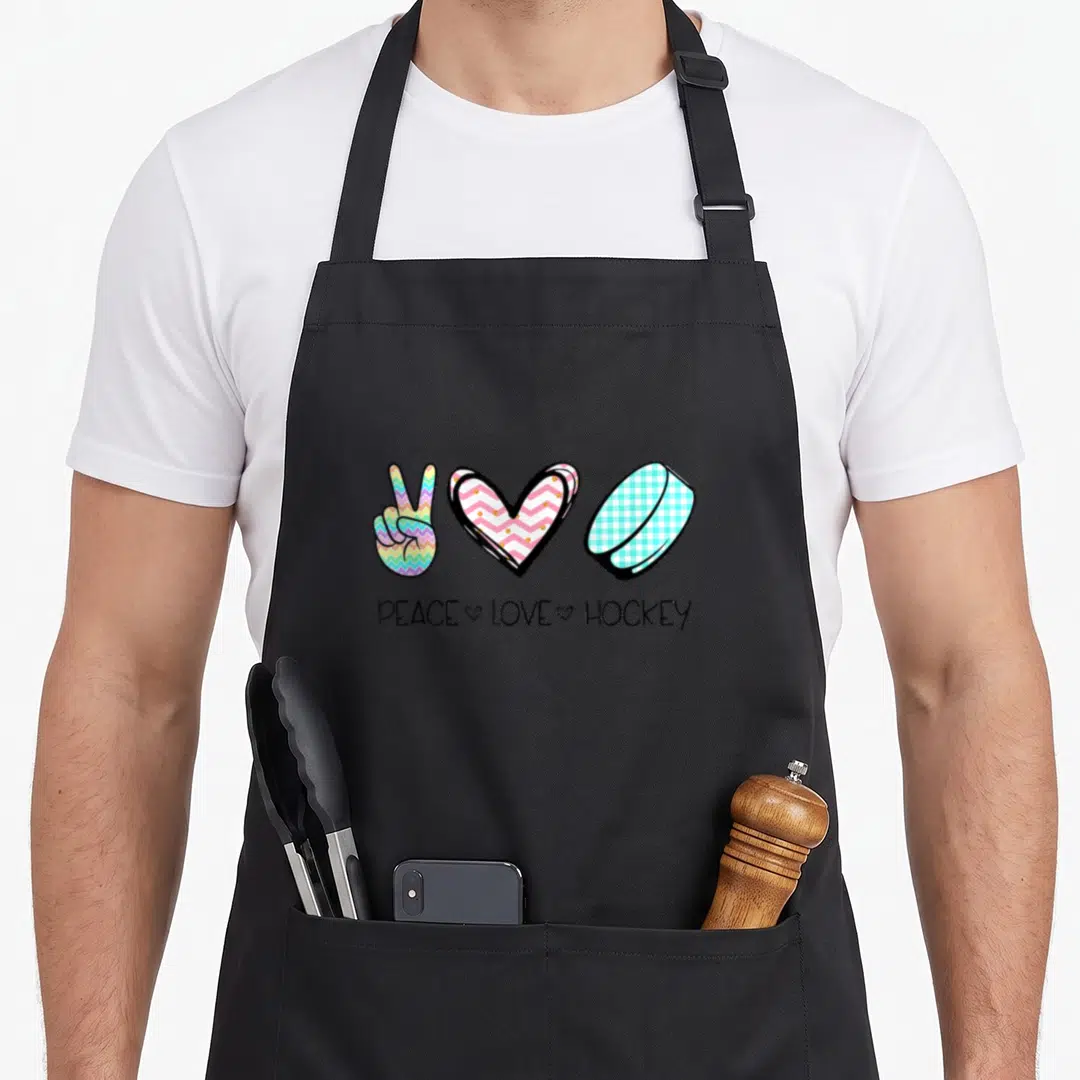Peace wintersport hockey apron - Peace sign heart and puck with text in rainbow chevron and gingham patterns — shown on a black cotton canvas apron against a white background