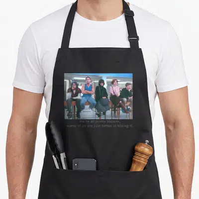 Breakfast pretty apron - Five people sitting on a fence with text We're all pretty bizarre below — shown on a black cotton canvas apron against a white background