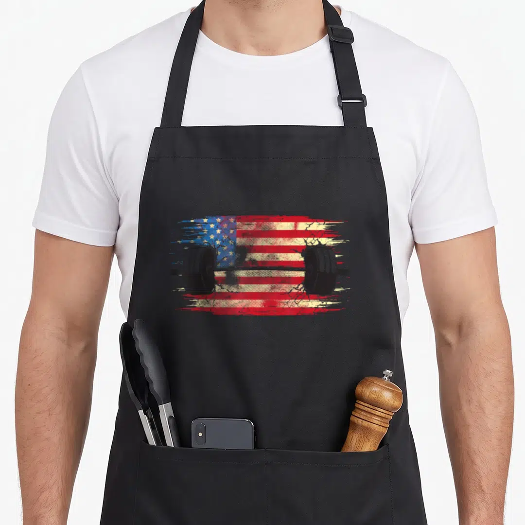 Gym american flag apron - Black barbell graphic over distressed red white and blue American flag pattern — shown on a black cotton canvas apron against a white background