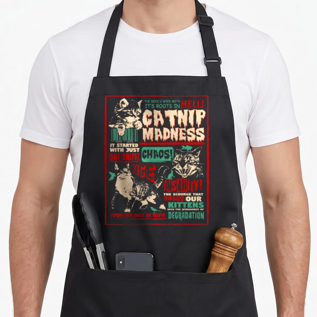 Madness funny cat aprons - Distressed catnip madness text with three cats and birds inside a red rectangular border — shown on a black cotton canvas apron against a white background