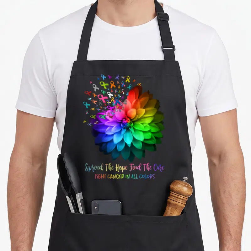 Fight find aprons - Realistic rainbow flower surrounded by red yellow green blue purple ribbons with hope cure text — shown on a black cotton canvas apron against a white background