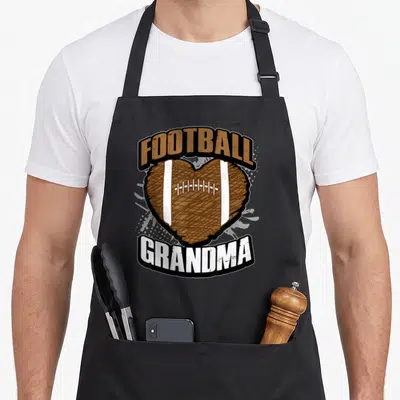 Jersey grandma aprons - Brown heart football with arched FOOTBALL GRANDMA text in cartoon style — shown on a black cotton canvas apron against a white background