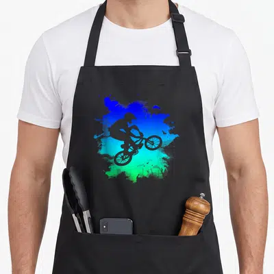 Bmx rider bike apron - Grey BMX rider silhouette jumping over blue and green paint splatter art — shown on a black cotton canvas apron against a white background