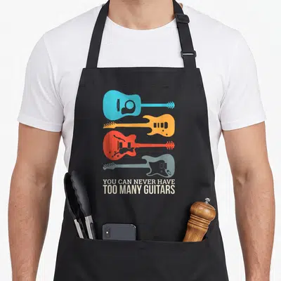 Many mkaur apron - Four stacked guitar silhouettes in blue, yellow, red, grey with white text reading You Can Never — shown on a black cotton canvas apron against a white background