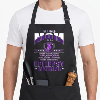 Proud warrior ribbon apron - Purple and white stacked text reading Proud Mom Epilepsy Warrior with ribbon and stars — shown on a black cotton canvas apron against a white background