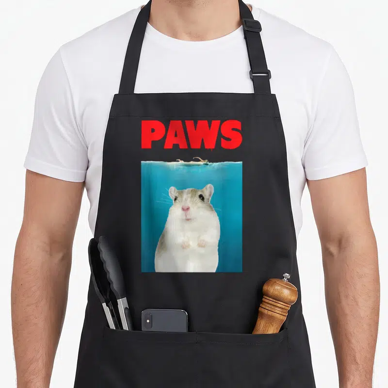 Paw gerbil lover apron - Red PAWS text above a white hamster swimming underwater in blue water — shown on a black cotton canvas apron against a white background