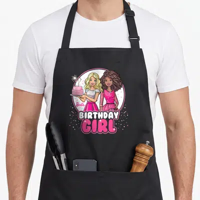 General bday apron - Two cartoon girls in pink circle holding cake with BIRTHDAY GIRL text and confetti — shown on a black cotton canvas apron against a white background