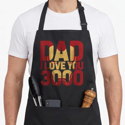 Fill father day apron - Red text DAD I LOVE YOU 3000 with gold Iron Man helmet behind — shown on a black cotton canvas apron against a white background