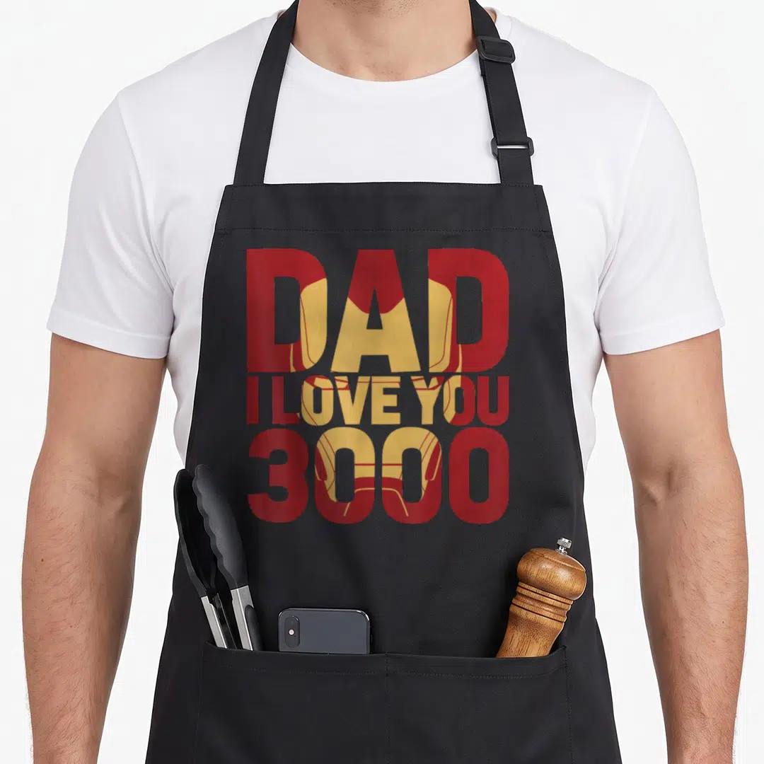 Fill father day apron - Red text DAD I LOVE YOU 3000 with gold Iron Man helmet behind — shown on a black cotton canvas apron against a white background