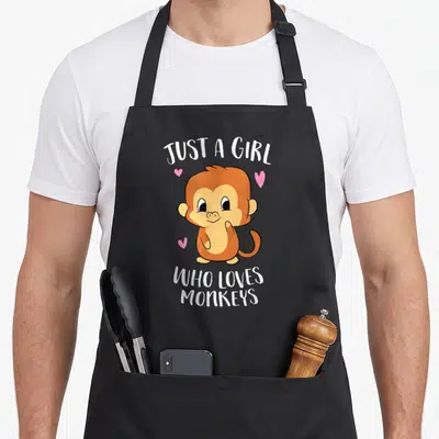 Retro monkey apron - Cartoon brown monkey with pink hearts and text JUST A GIRL WHO LOVES MONKEYS — shown on a black cotton canvas apron against a white background