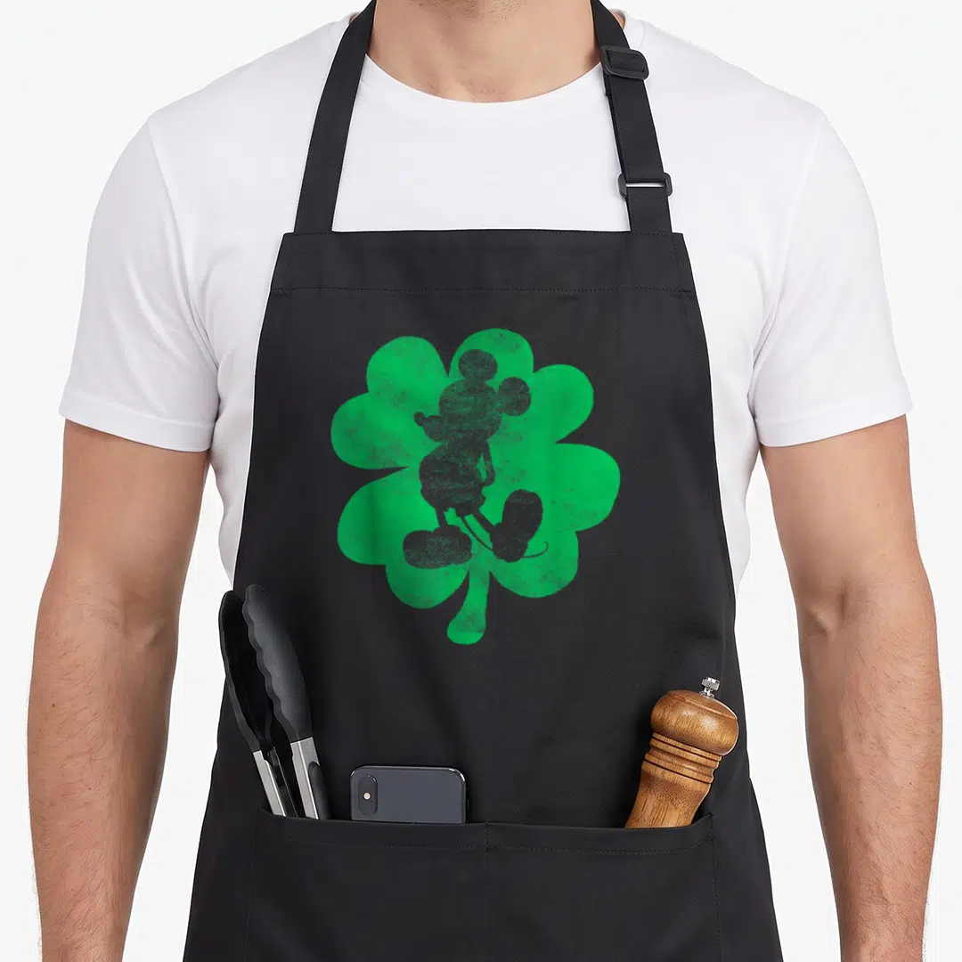Shamrock mice looks apron - Grey Mickey Mouse silhouette inside a green distressed shamrock — shown on a black cotton canvas apron against a white background