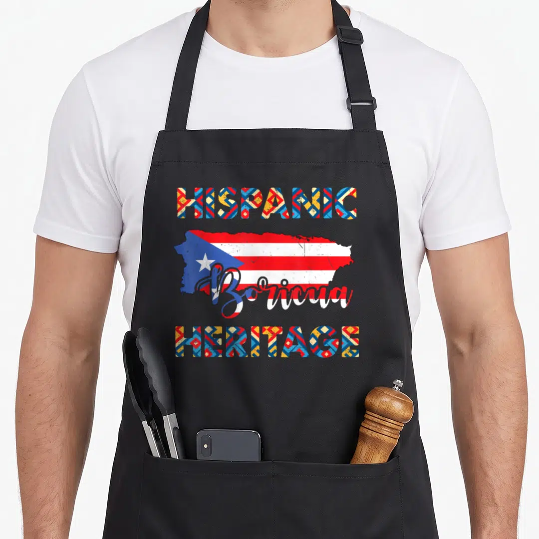 Rico hispanic aprons - Puerto Rico map shape with Boricua script and geometric HISPANIC HERITAGE text in red white blue — shown on a black cotton canvas apron against a white background