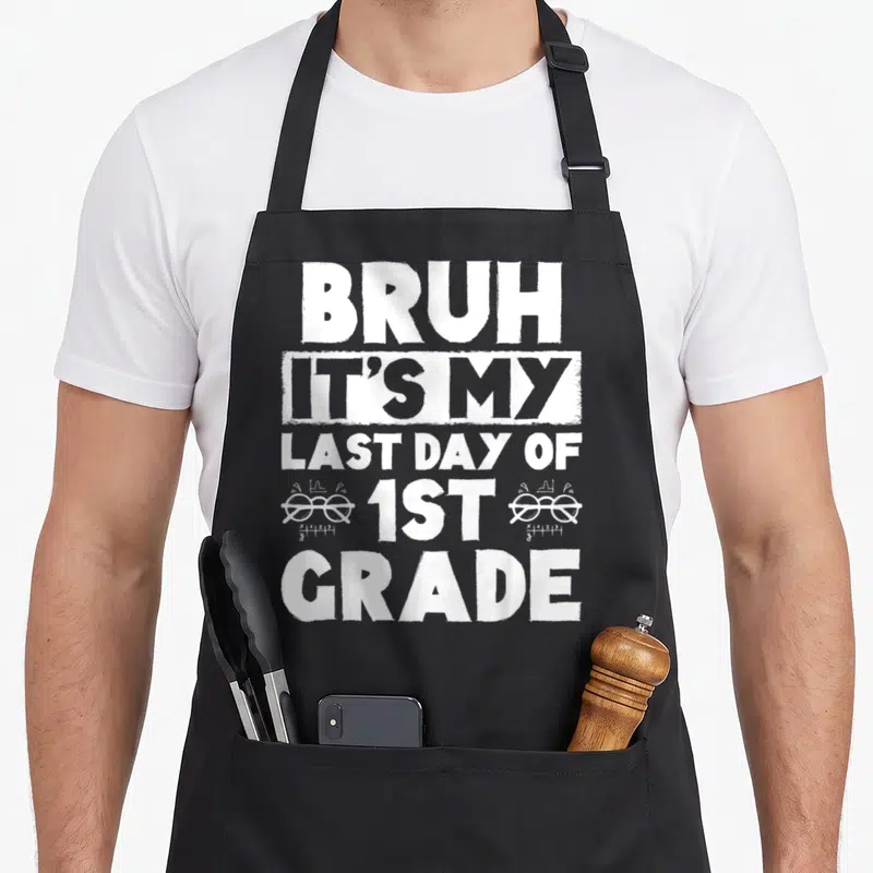 Grade summer teacher apron - Stacked white distressed text reading Bruh It's My Last Day Of 1st Grade with math graphs — shown on a black cotton canvas apron against a white background
