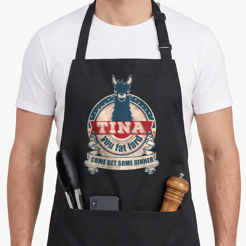 Lard fat man in apron - Blue llama head in circular emblem with red TINA banner and cream ribbon reading come get some — shown on a black cotton canvas apron against a white background