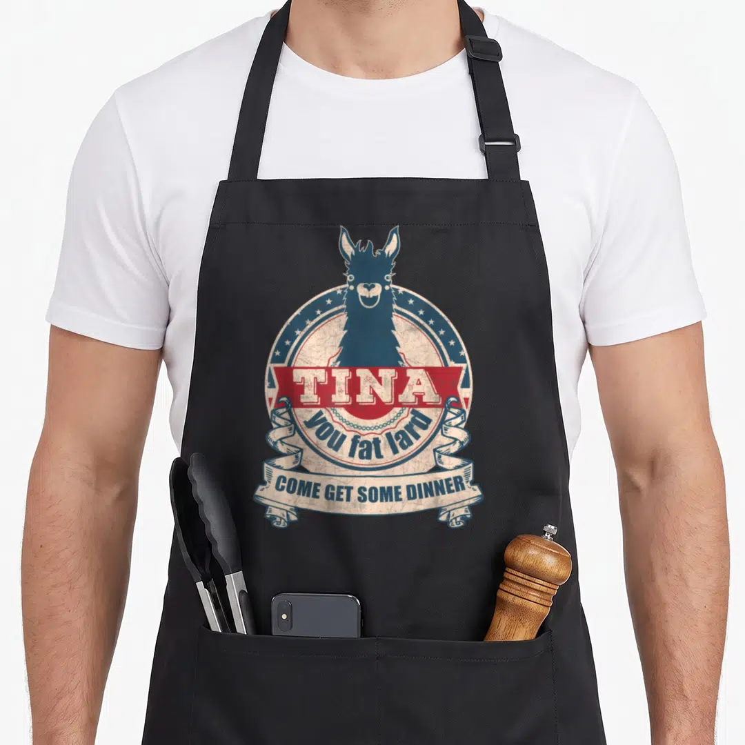 Lard fat man in apron - Blue llama head in circular emblem with red TINA banner and cream ribbon reading come get some — shown on a black cotton canvas apron against a white background