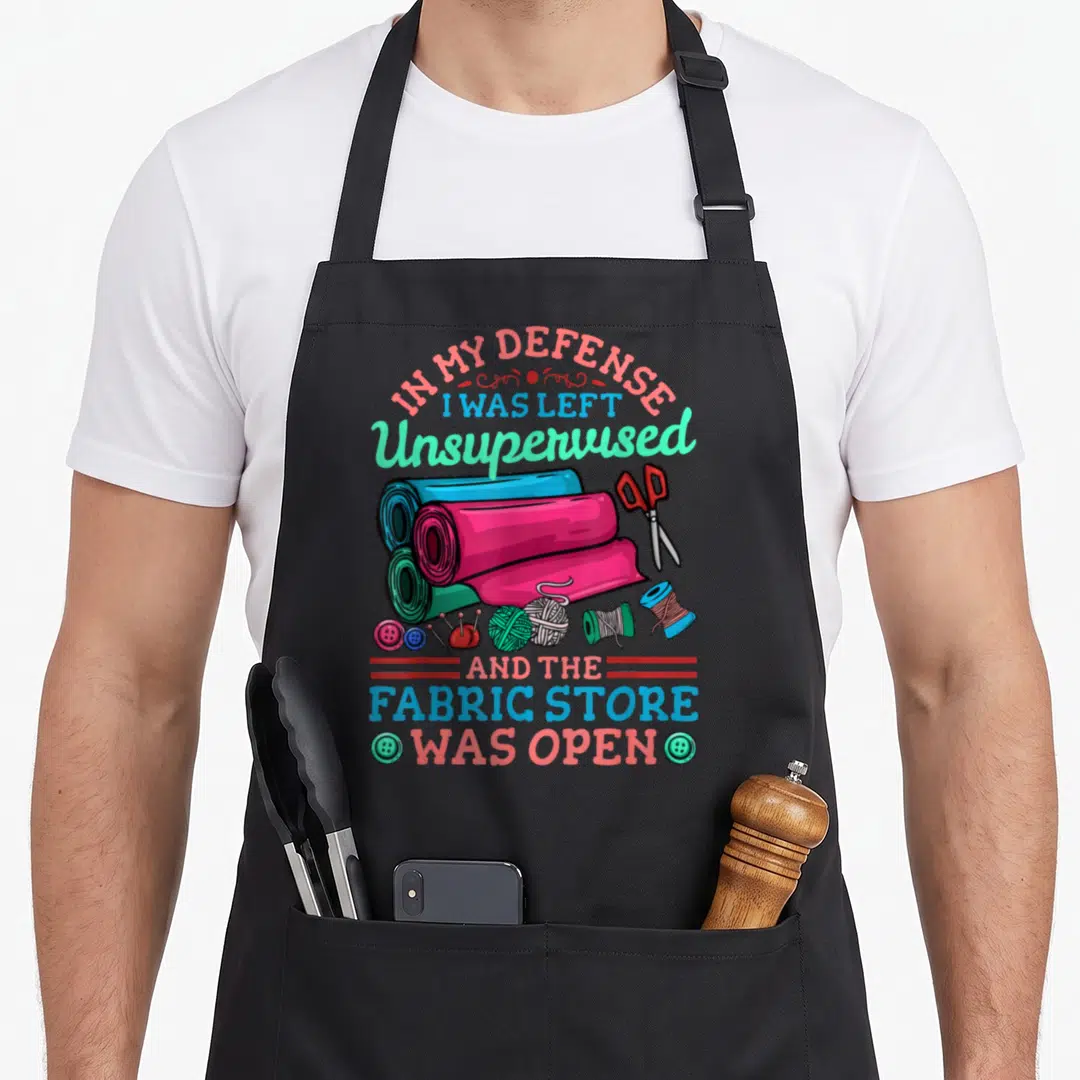 Quilting quilter apron - Cartoon fabric rolls and sewing supplies with text about being left unsupervised at a fabric — shown on a black cotton canvas apron against a white background