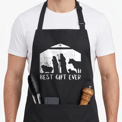 Nativity xmas christmas apron - White distressed nativity silhouette inside stable shape with BEST GIFT EVER text below — shown on a black cotton canvas apron against a white background