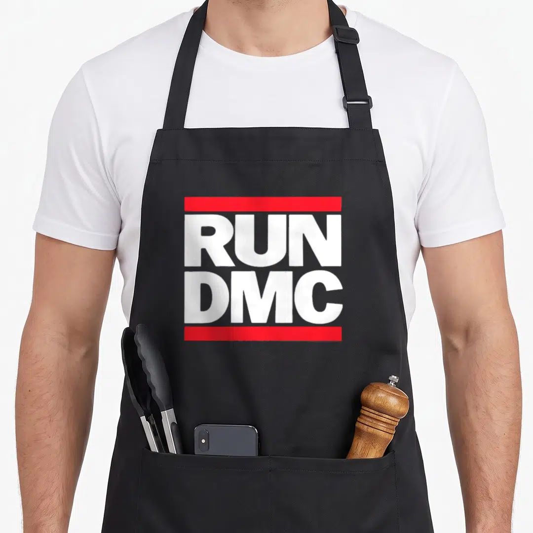 Funny run dmc apron - White RUN DMC text sandwiched between two horizontal red bars — shown on a black cotton canvas apron against a white background