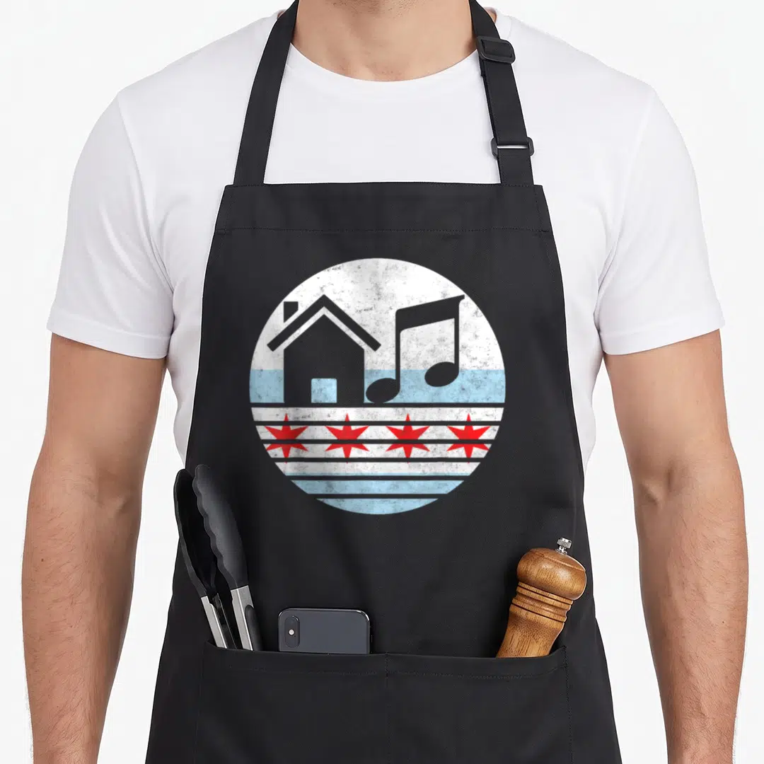 Edm chicago apron - Circular distressed graphic with grey house, musical note, and four red stars on blue and white — shown on a black cotton canvas apron against a white background
