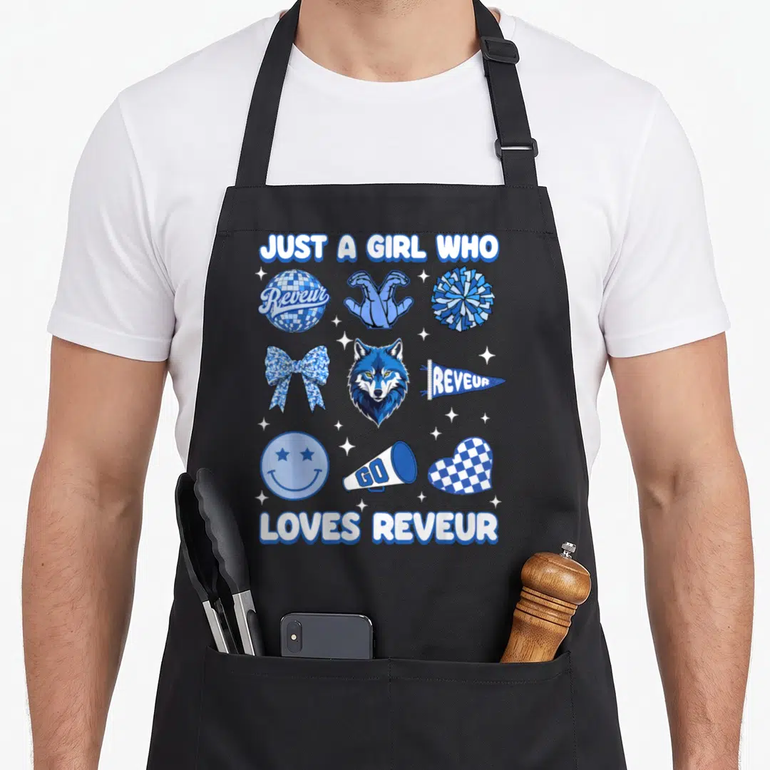 Reveur dreamer apron - Blue wolf head surrounded by pom poms, megaphone, and checkerboard patterns with text — shown on a black cotton canvas apron against a white background