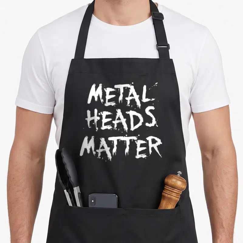 Band heavy apron - White stacked text reading METAL HEADS MATTER on grey background — shown on a black cotton canvas apron against a white background
