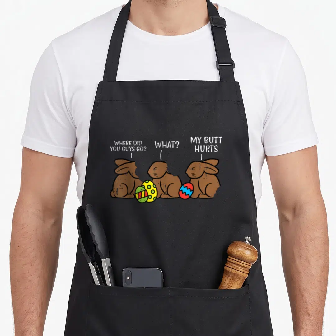 Chocolate easter bunny aprons - Three cartoon rabbits with speech bubbles and colorful eggs printed on fabric — shown on a black cotton canvas apron against a white background