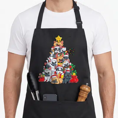Christmas french apron - Pyramid of French Bulldogs in Santa hats and scarves topped with yellow star surrounded by red — shown on a black cotton canvas apron against a white background