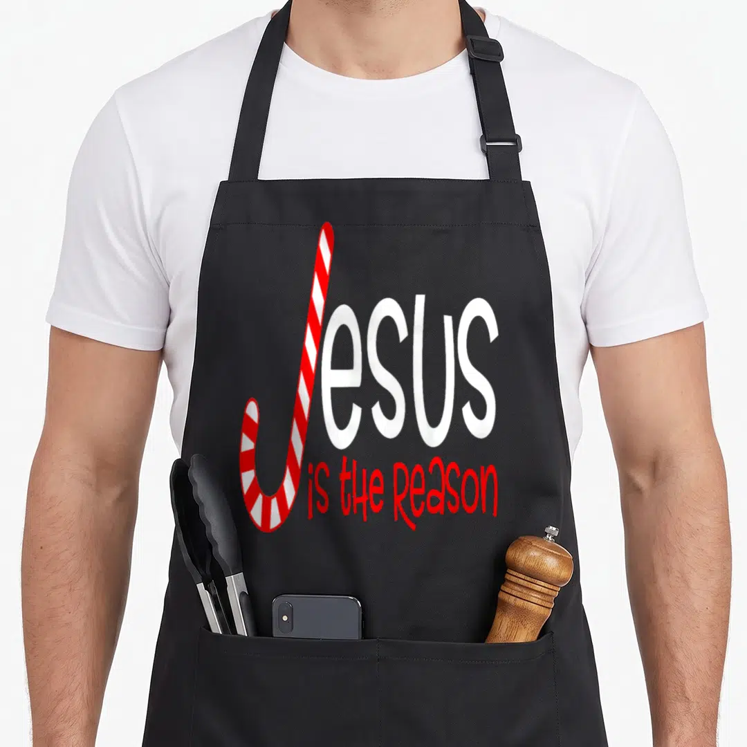 Jesus candy cane apron - Red and white candy cane forming J in Jesus is the Reason text — shown on a black cotton canvas apron against a white background