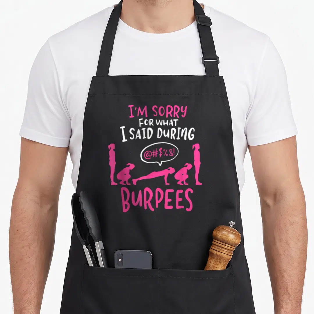 Sorry gym burpees apron - Pink and white text above five female silhouettes doing burpees with speech bubble — shown on a black cotton canvas apron against a white background