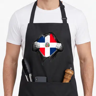 Dominican dominica apron - Flag seen through jagged hole in grey surface with two hands gripping edges — shown on a black cotton canvas apron against a white background