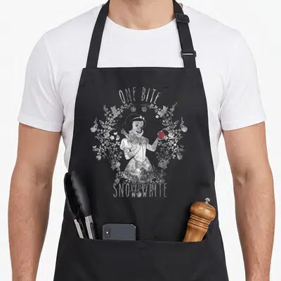 Bite apple apron - Snow White holding red apple inside white floral wreath with arched text ONE BITE — shown on a black cotton canvas apron against a white background