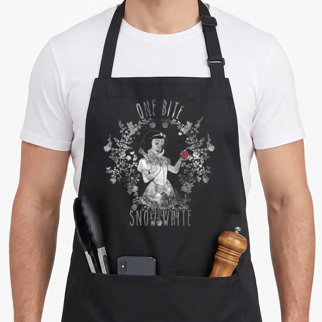 Bite apple apron - Snow White holding red apple inside white floral wreath with arched text ONE BITE — shown on a black cotton canvas apron against a white background