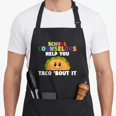 Counseling mexican apron - Smiling cartoon taco surrounded by multi-colored text reading SCHOOL COUNSELORS HELP YOU — shown on a black cotton canvas apron against a white background