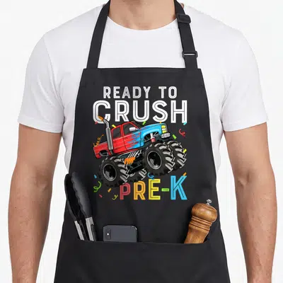 Pre preschool truck apron - Cartoon monster truck with confetti and text READY TO CRUSH PRE-K — shown on a black cotton canvas apron against a white background
