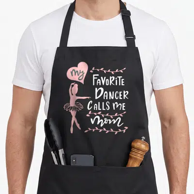 Meme mother's apron - Pink ballerina silhouette next to stacked white text reading my FAVORiTe DANCER CALLS me mom — shown on a black cotton canvas apron against a white background