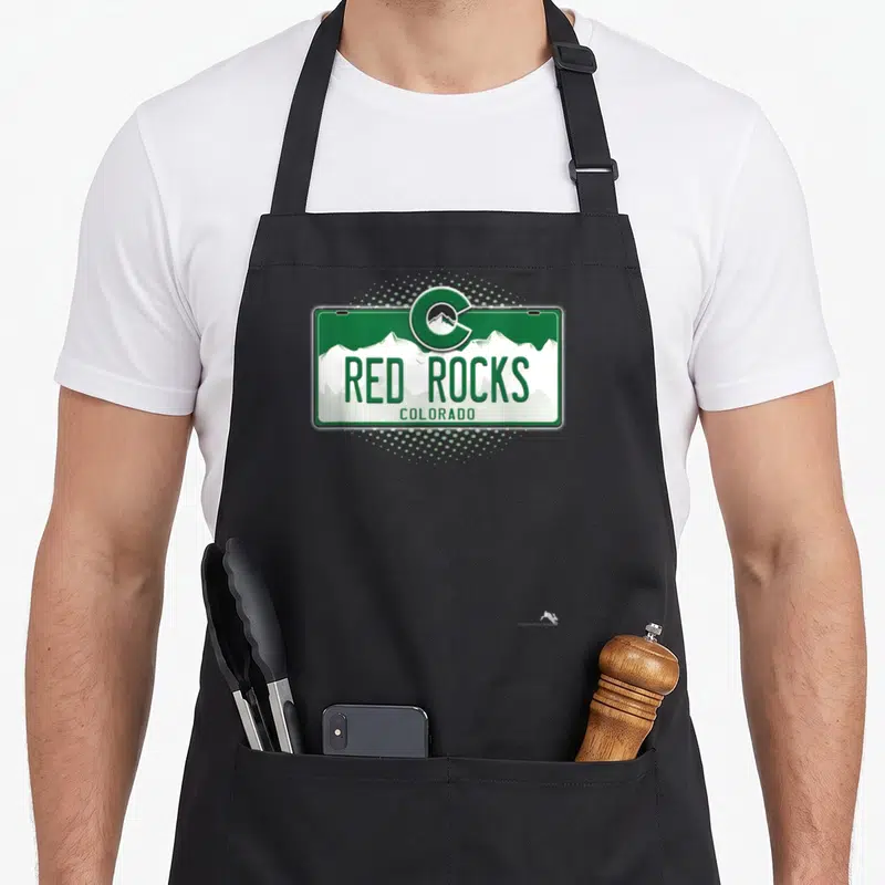 License colorado apron - Green and white Red Rocks Colorado license plate with mountain C logo on dotted background — shown on a black cotton canvas apron against a white background