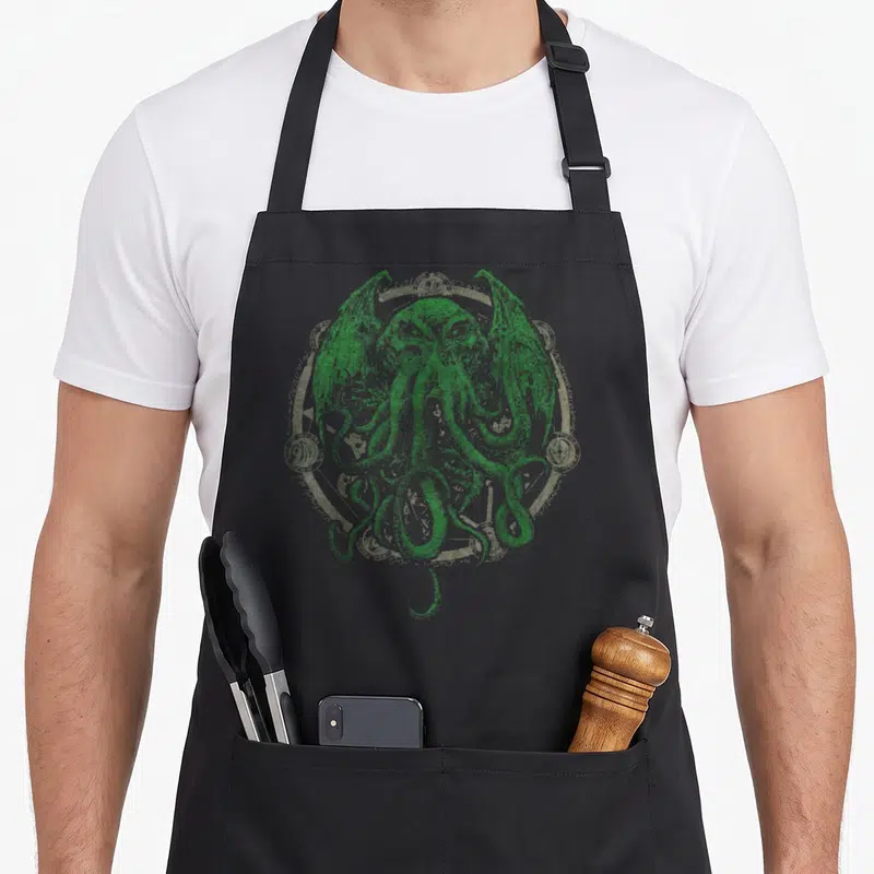 Cthulhu horror apron - Green and grey line art of Cthulhu with tentacles and wings inside a circular ornate frame — shown on a black cotton canvas apron against a white background