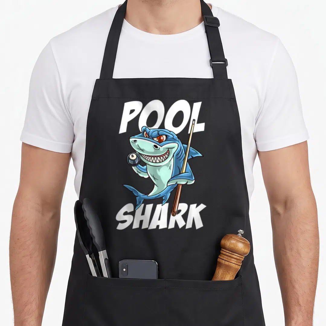 Billiard joke apron - Cartoon blue shark holding 8-ball and cue with POOL SHARK text — shown on a black cotton canvas apron against a white background