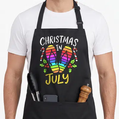 July summer christmas vacation apron - Rainbow flip flops flanked by candy canes and holly under arched Christmas — shown on a black cotton canvas apron against a white background