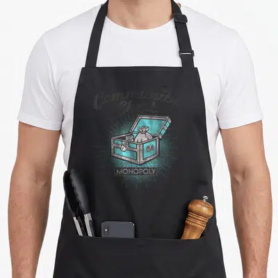 Community monopoly apron - Distressed treasure chest with Community Chest text and Since 1935 logo — shown on a black cotton canvas apron against a white background