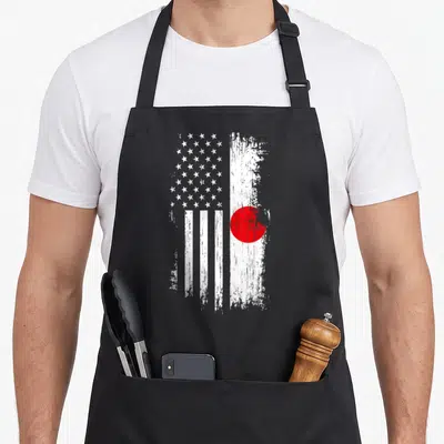 Japanese american flag apron - Distressed hybrid flag with white stars, vertical stripes, and a red circle on a white — shown on a black cotton canvas apron against a white background