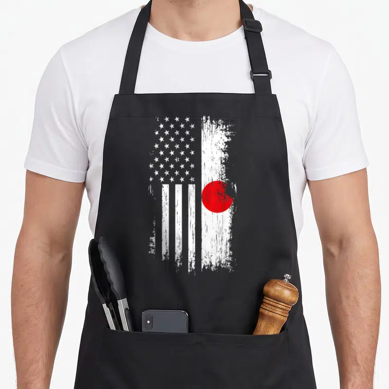 Japanese american flag apron - Distressed hybrid flag with white stars, vertical stripes, and a red circle on a white — shown on a black cotton canvas apron against a white background