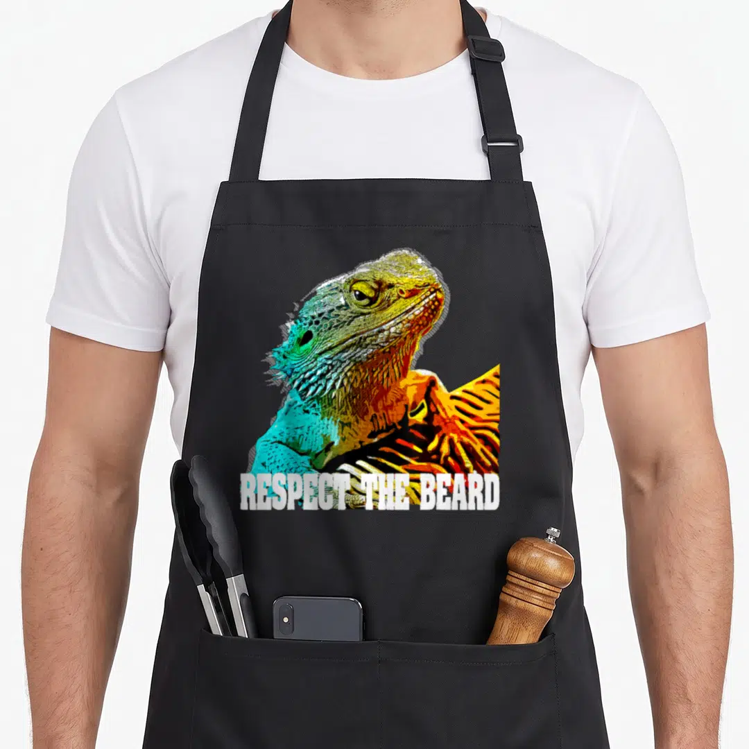 Bearded beard apron - Colorful bearded dragon head with white RESPECT THE BEARD text across the bottom — shown on a black cotton canvas apron against a white background