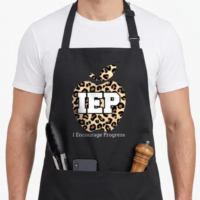 Progress iep teacher apron - Leopard print apple with IEP text and I Encourage Progress caption — shown on a black cotton canvas apron against a white background