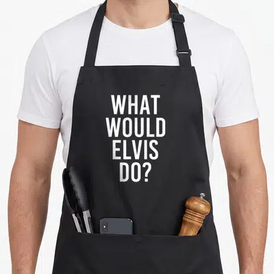 Would joke apron - White stacked text reading WHAT WOULD ELVIS DO? on grey fabric — shown on a black cotton canvas apron against a white background