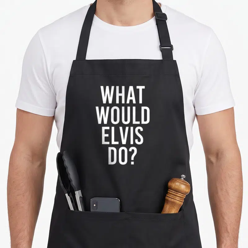 Would joke apron - White stacked text reading WHAT WOULD ELVIS DO? on grey fabric — shown on a black cotton canvas apron against a white background